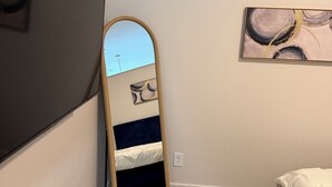 Un dormitorio con una cama, un espejo, una obra de arte en la pared y suelo de madera.