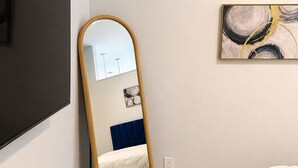 Un dormitorio con cama, un espejo grande, un cuadro y un televisor montado en la pared.