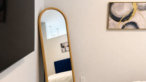 A bedroom with a bed, a large mirror, a painting, and a TV mounted on the wall.