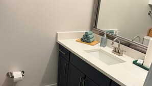 A bathroom with a white sink, dark cabinets, a green rug, and a wicker basket.