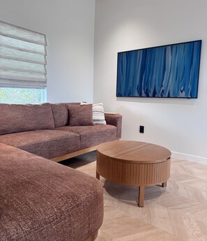 Ein modernes Wohnzimmer mit einem Ecksofa, einem runden Holztisch und einem großen abstrakten Gemälde an der Wand.