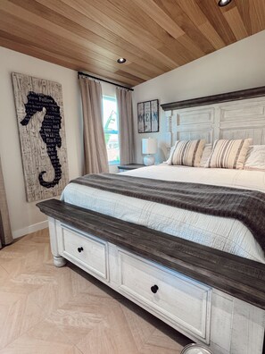 Ein Schlafzimmer mit Holzbalkendecke, einem Bett mit gestreifter Bettwäsche, einer weißen Kommode mit Schubladen und einem Wandbild mit einem Seepferdchen.