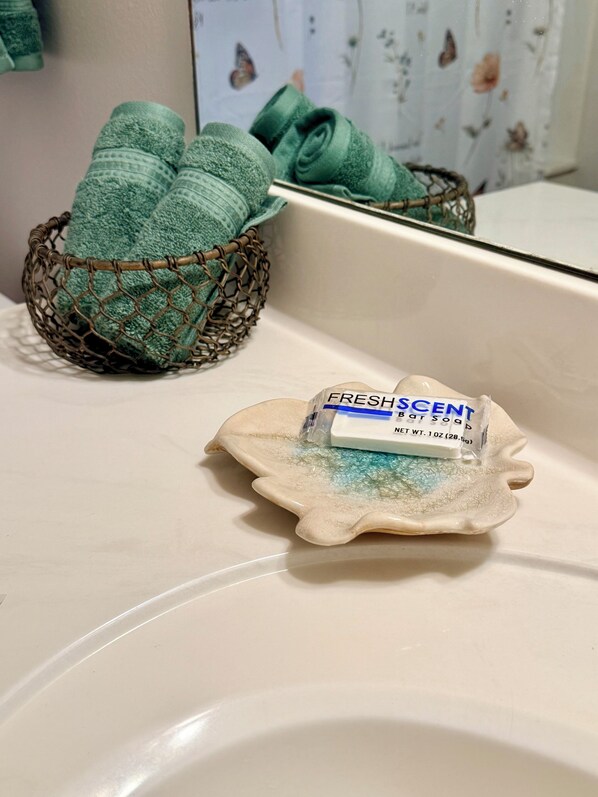 Un lavandino in bagno con una saponetta etichettata 'FRESH SCENT' e un cesto in filo con asciugamani piegati.