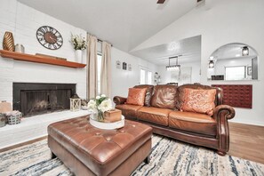 Ein Wohnzimmer mit Kamin, Ledersofa, Hocker und einer Wanduhr.