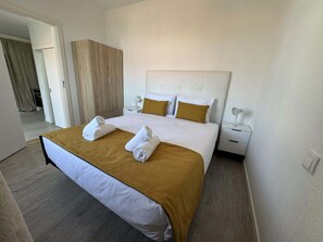 Ein Hotelzimmer mit einem Bett, zwei Kissen, einem Nachttisch, einer Lampe und einer Tür zu einem weiteren Raum.