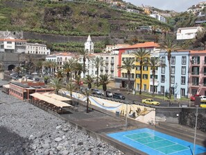 A coastal town with buildings, a beach, and a blue tennis court. - Atlantic Villa Sunset – Cozy Island Stay – 1 bedroom (Ponta do Sol)