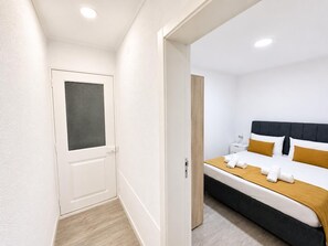 Quarto de hotel com cama, mesa de cabeceira e porta com veneziana.
