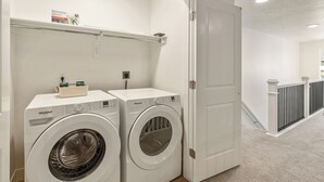 Una sala amb bugaderia, amb dues rentadores Whirlpool, una estant plena de productes de bugaderia i una porta que dona a un passadís.