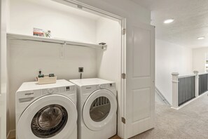 A laundry room with two Whirlpool washers, a shelf with laundry supplies, and a door leading to a hallway. - Riverpoint Retreat, Pool and Gym, Near Utah Lake, New Build (Lehi)
