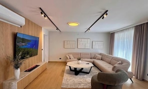 Ein modernes Wohnzimmer mit einem Ecksofa, einem Flachbildfernseher, einem Couchtisch und abstrakter Wandkunst.