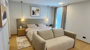 Et moderne soveværelse med seng, sengeborde, en sofa, et tæppe og et billede på væggen.