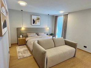 Ein modernes Schlafzimmer mit Bett, Nachttischen, einer Couch, einem Teppich und einem Bild an der Wand.