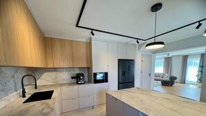 Een moderne keuken met een marmeren aanrecht, een ingebouwde koffiemachine en een zwarte koelkast.