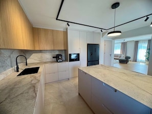Eine moderne Küche mit Marmorarbeitsplatte, integrierter Kaffeemaschine und einem schwarzen Kühlschrank.