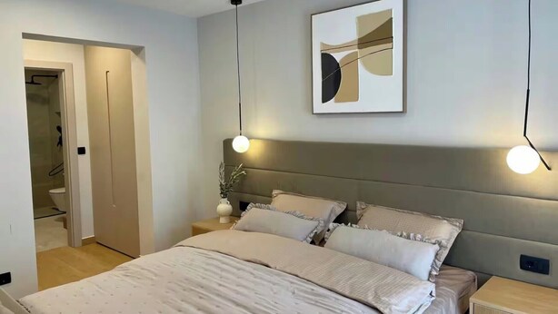 Een moderne slaapkamer met een bed, nachtkastjes, een abstract kunstwerk aan de muur en een deur naar de badkamer.