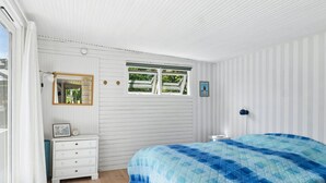 Ein Schlafzimmer mit Bett, Kommode, Spiegel und Fenster.