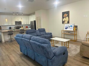 A modern living room with a blue sectional sofa, a small white table, and a kitchen in the background. - 3-bedroom house near NRG Stadium, Texas Med. Center...in the heart of Houston (Houston)