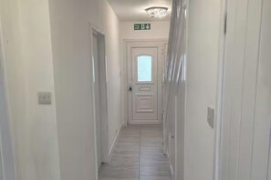 A narrow hallway with white walls, a light-colored tiled floor, and a door at the end. - House Sleeps 7 with Garden and Parking (Erith)
