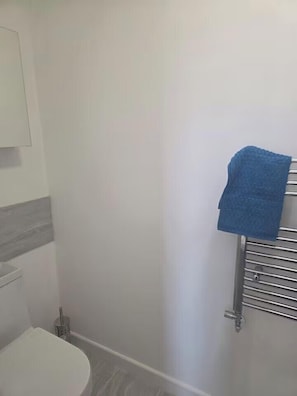 Ein Badezimmer mit Toilette, Handtuchhalter mit blauem Handtuch und Duschbereich.