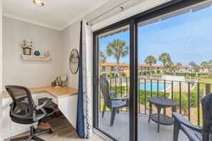 A balcony with a pool, a desk with a chair, and a view of a residential area. - Walk to Beach, Two Pools, King Suite — Sleeps 6 (St. Augustine)