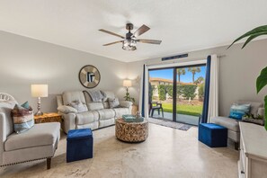 A living room with a ceiling fan, a sofa, a coffee table, and a view through a sliding glass door.