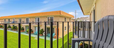 A balcony with a view of a building with a tiled roof, a fenced yard, and outdoor furniture.