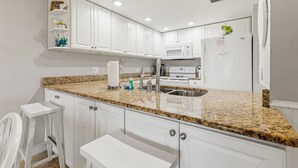 Cucina con mobili bianchi, piani di lavoro in granito, lavello in acciaio inox, microonde e frigorifero.
