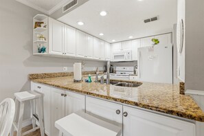 A kitchen with white cabinets, granite countertops, a stainless steel sink, a microwave, and a refrigerator. - Walk to Beach, Two Pools, King Suite — Sleeps 6 (St. Augustine)