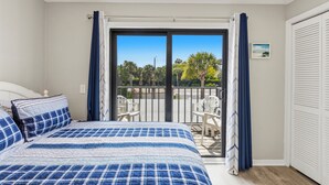 Una camera da letto con un letto, un balcone con sedie e vista su alberi e un edificio.