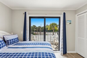 A bedroom with a bed, a balcony with chairs, and a view of trees and a building. - Walk to Beach, Two Pools, King Suite — Sleeps 6 (St. Augustine)