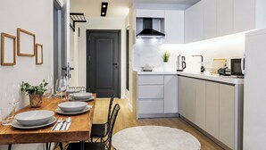 A modern kitchen with white cabinets, a black stove hood, and a dining area with a wooden table and chairs. - Gorgeous 3 Bedroom Apartment At Monnas Suite (Beyoglu)
