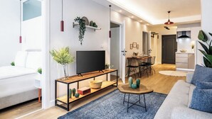 A modern living room with a sofa, a TV, a dining area with chairs, and a kitchen in the background. - Gorgeous 3 Bedroom Apartment At Monnas Suite (Beyoglu)