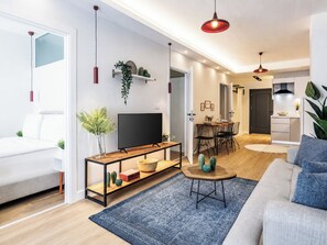 A modern living room with a sofa, a TV, a dining area with chairs, and a kitchen in the background. - Gorgeous 3 Bedroom Apartment At Monnas Suite (Beyoglu)