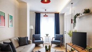 Een moderne woonkamer met een bank, twee fauteuils, een salontafel, een televisie en een bijzettafeltje.
