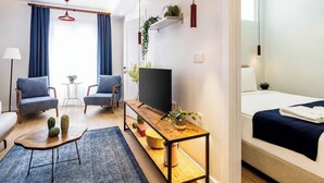 Een moderne hotelkamer met een bank, twee fauteuils, een televisie, een houten bijzettafeltje en een bed.