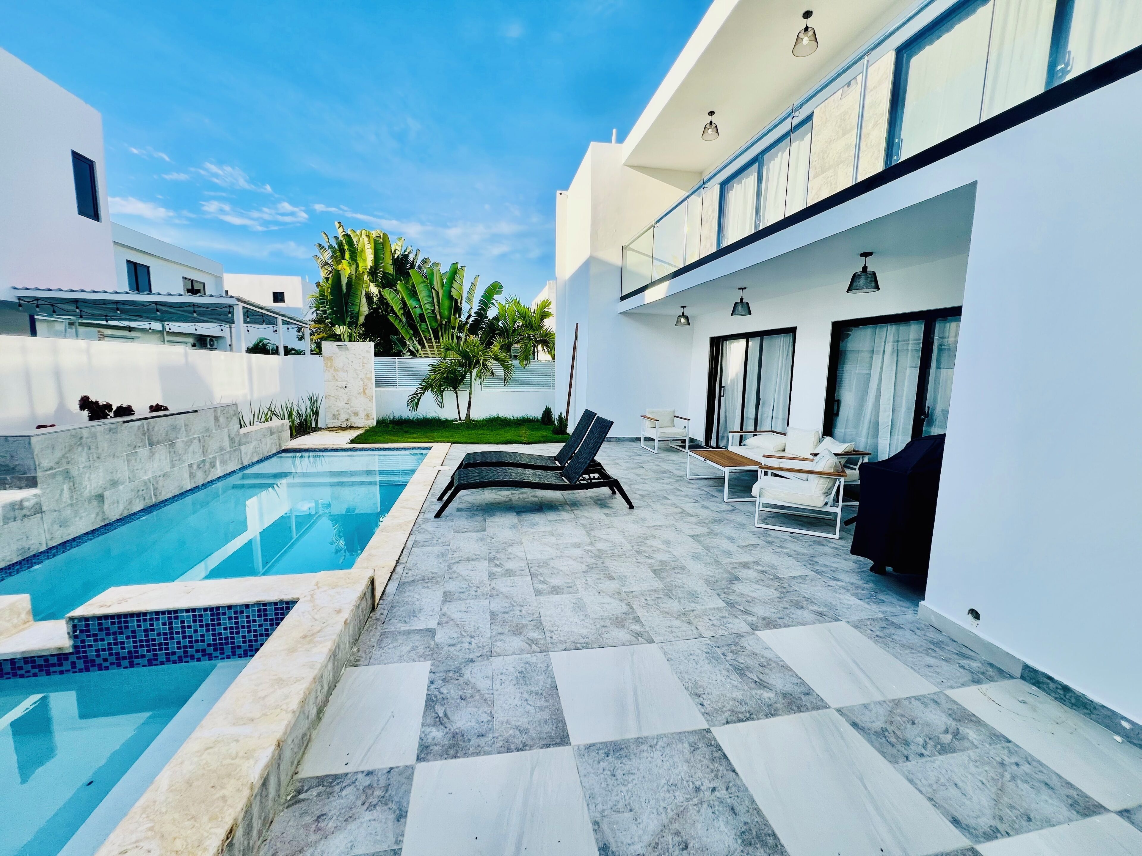 A modern outdoor pool area with a checkered floor, lounge chairs, and a glass balustrade.