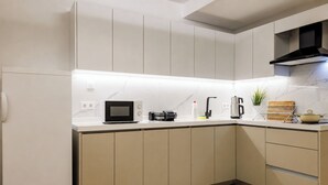 Eine moderne Küche mit weißen Schränken, einer Mikrowelle, einer Kaffeemaschine und einem kleinen Topf mit Pflanze.