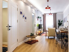A modern living room with a wooden floor, a TV stand, a sofa, a dining table set for six, and a small side table with a vase. - Glamorous Cihangir 3 Bedrooms Apt At Monnas Suite (Beyoglu)