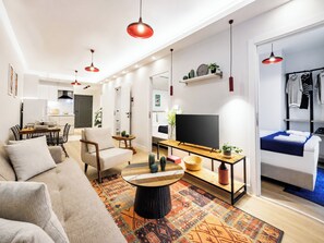 Ein modernes Wohnzimmer mit Sofa, Couchtisch, Fernseher und einem Essbereich mit Stühlen und Tisch.
