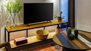 Uma sala de estar moderna com televisão de tela plana, mesa de console de madeira, mesa de centro redonda, tapete estampado e uma planta de cacto.