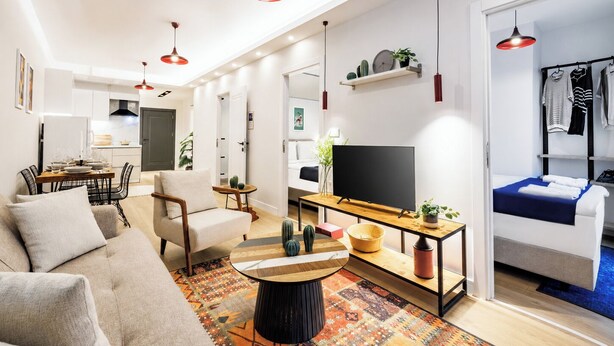 Ein modernes Wohnzimmer mit Sofa, Couchtisch, Fernseher und einem Essbereich mit Stühlen und Tisch.