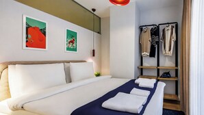 Ein Hotelzimmer mit einem Bett, einem Kleiderschrank, einem Regal mit Kleidung und zwei Wandbildern.