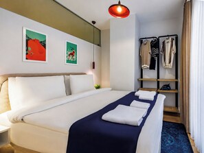 Ein Hotelzimmer mit einem Bett, einem Kleiderschrank, einem Regal mit Kleidung und zwei Wandbildern.