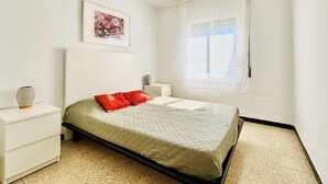 Un dormitorio con cama, mesita de noche, ventana con cortinas y un cuadro enmarcado en la pared.