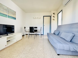 A living room with a TV, a grey sofa, a dining table with chairs, and a door. - LUXEMBURG. Zona quiet on the Costa Brava (Roses)