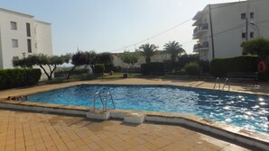 Una piscina con plataforma de baldosas, rodeada de edificios y vegetación.