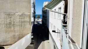 Un estrecho callejón entre edificios, con vista despejada a una playa y palmeras en la distancia.