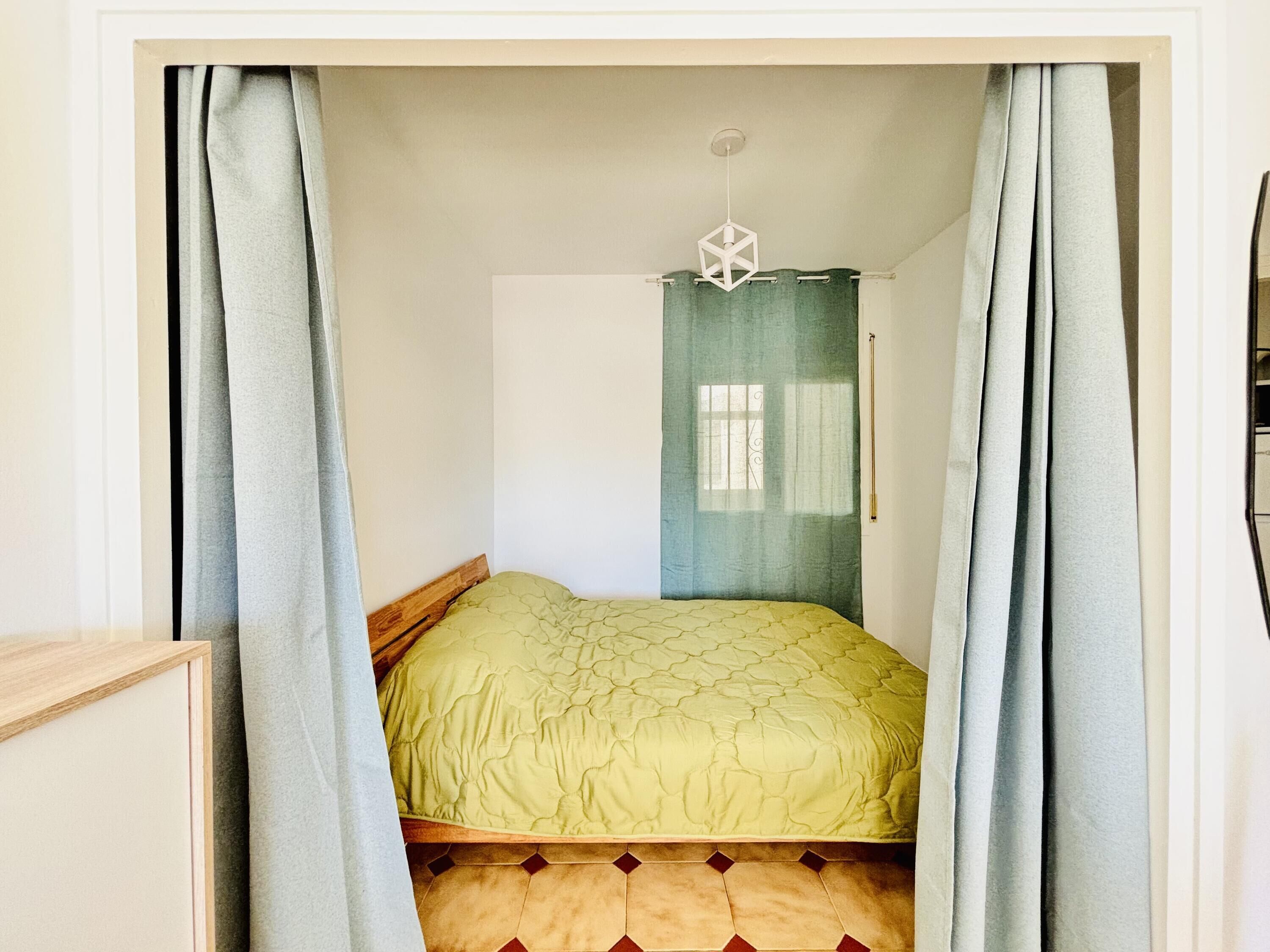 Quarto com cama, cortinas, janela com cortina e luminária no teto.