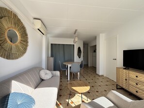 Ein modernes Wohnzimmer mit einer Couch, einem kleinen Tisch, einem Fernseher und einem Essbereich mit Stühlen.