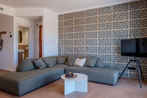 A modern living room with a sectional sofa, a small round coffee table, a TV on a tripod stand, and a decorative wall panel. - Completely renovated house with pool and sea views in Aiguablava (Begur)